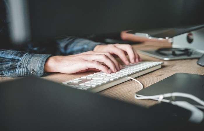 A person typing on a white keyboard at a wooden desk